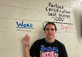  Cameron LaDuke stands pointing to perfect score inscribed on wall.